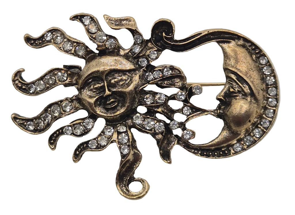 An antique-style brooch featuring a sun and crescent moon design, embellished with clear rhinestones on a gold-toned metal background.