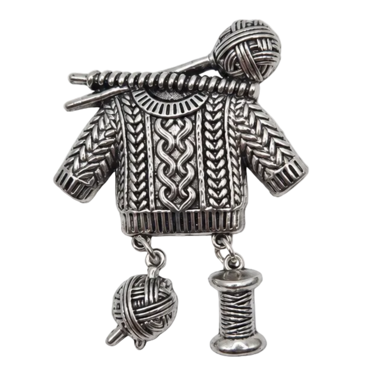 A silver-toned metal brooch shaped like a knitted sweater with knitting needles and yarn balls, shown on a plain white background.