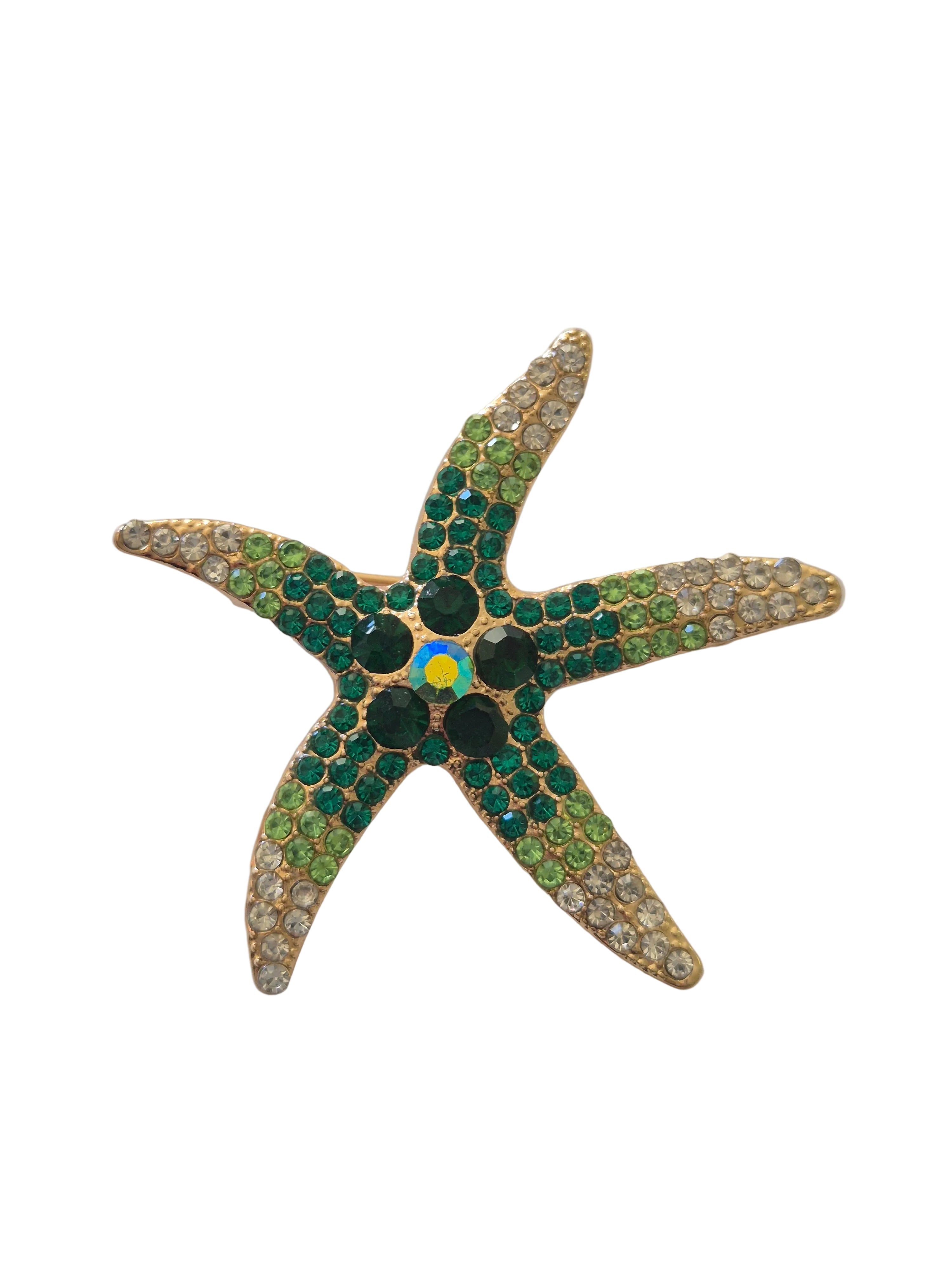 Starfish-shaped brooch with green gemstones and a blue center on a white background