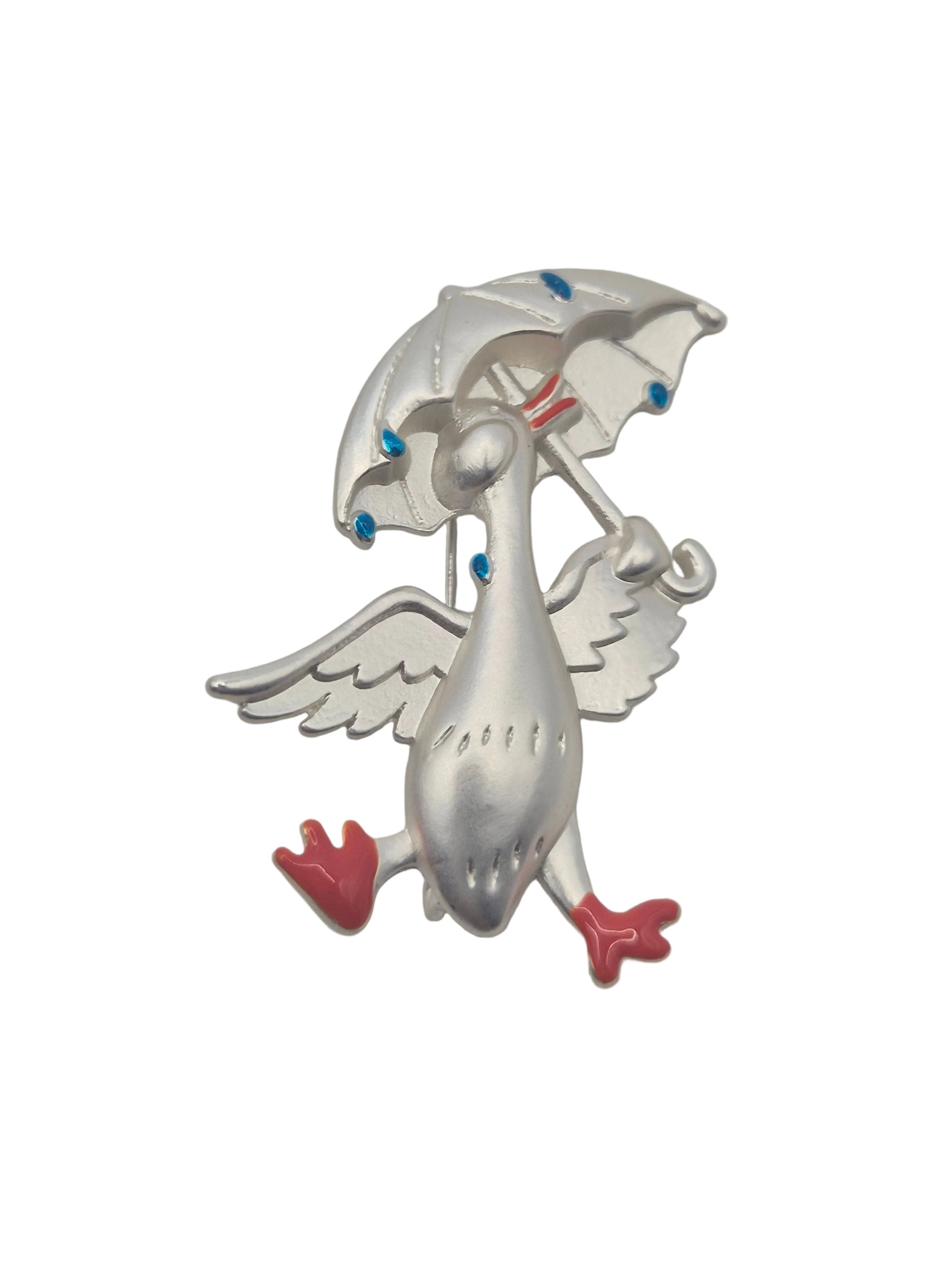 Silver tone metal duck holding an umbrella brooch with raindrops on a plain white background 