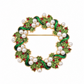 A circular gold-tone brooch designed as a holly wreath, featuring green enamel leaves, white faux pearls, and small red crystal accents on a plain white background.