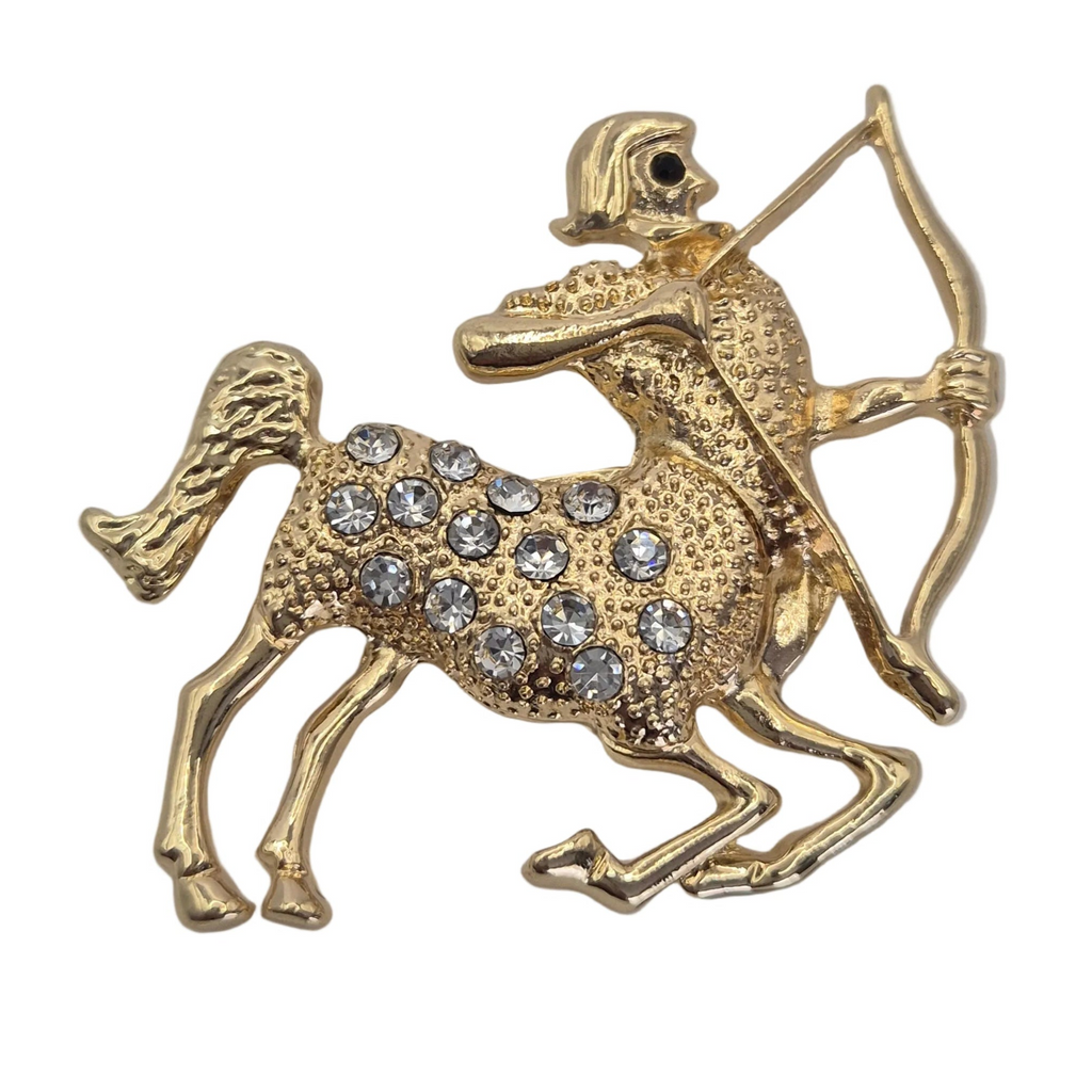 A gold-tone brooch shaped like a centaur horse with a rider aiming a bow, embellished with clear rhinestones on its body, set against a plain white background.