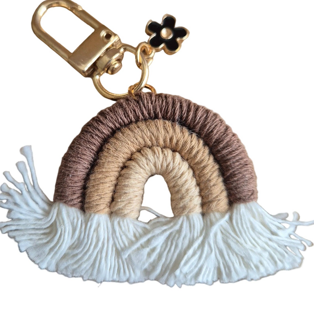 A handmade woven rainbow keychain with white tassels and a gold-tone clasp. The rainbow is made of three horizontal bands of brown, beige, and white yarn, with white tassels hanging from the bottom.