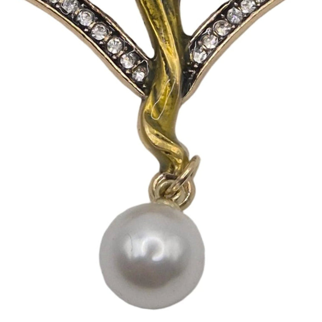 An Art Deco style brooch featuring a winged fairy figure with blue and gold enamel details, set with clear rhinestones and hanging from a white pearl drop, shown on a plain white background.