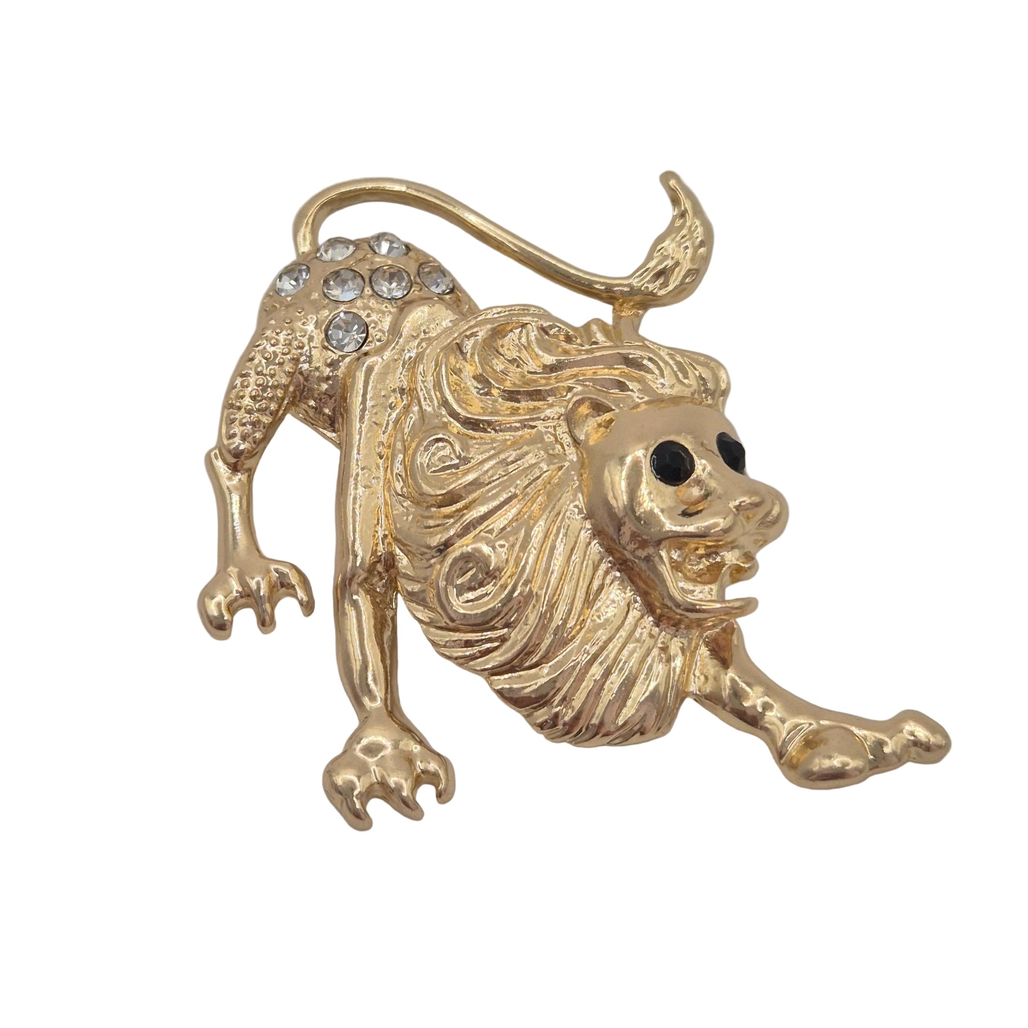 A gold lion figurine brooch with a textured mane, black eyes, embellished with clear rhinestones on its hindquarters, shown on a plain light gray background.