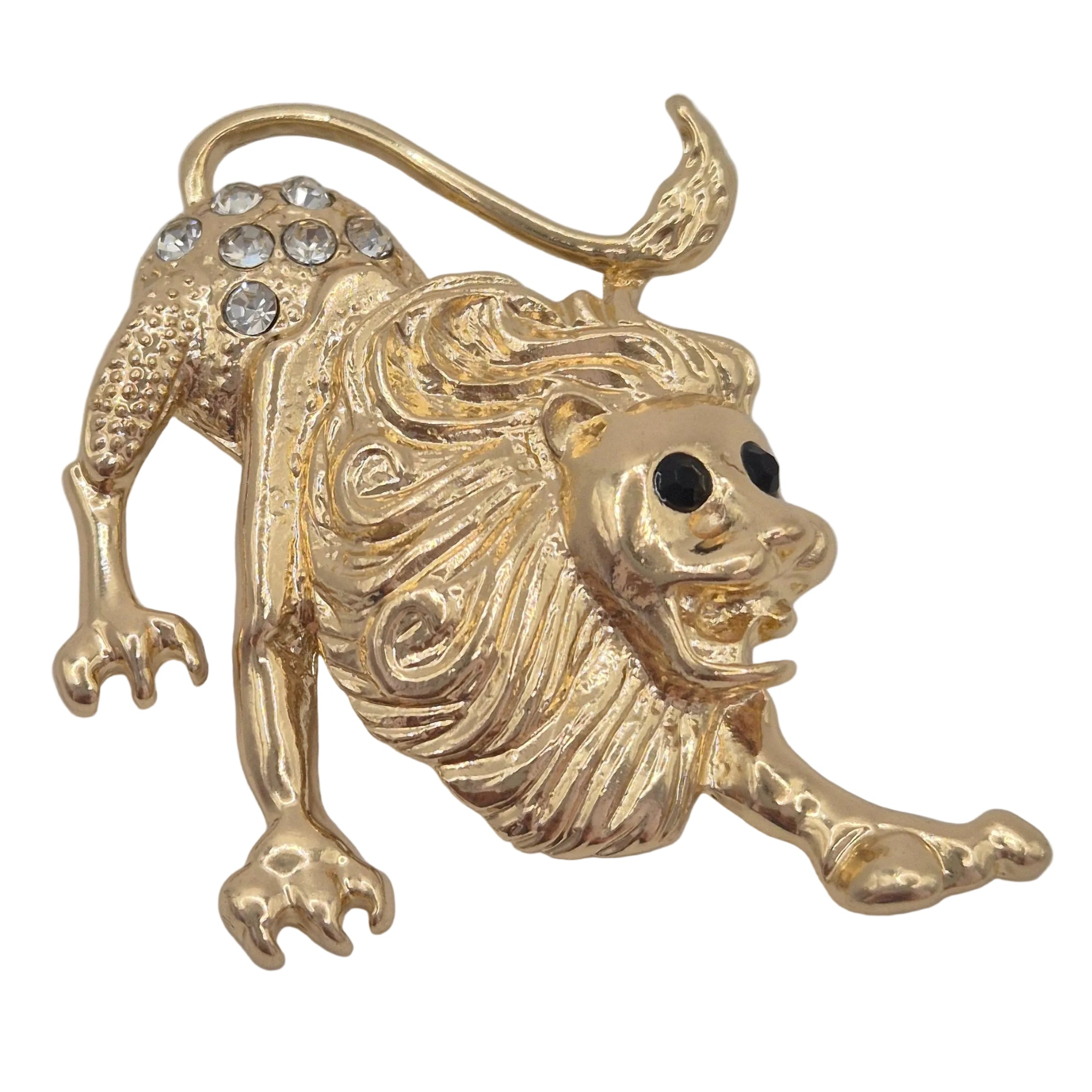 A gold lion figurine brooch or pin, shown in a crawling pose with a tail, detailed mane, black eyes, and clear rhinestones on its back, set against a plain white background.