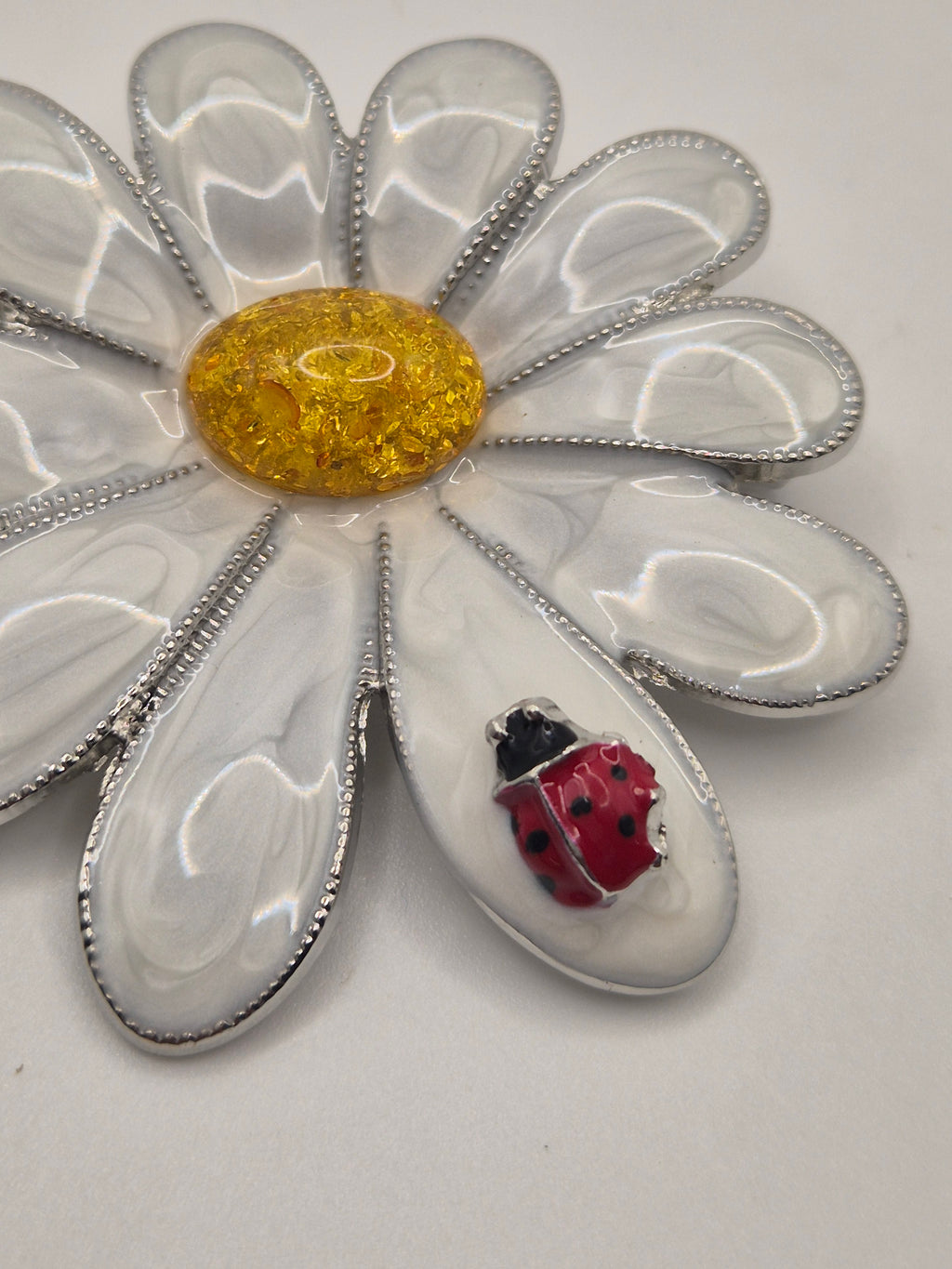 Brooch shaped like a daisy with a ladybug on a gray background