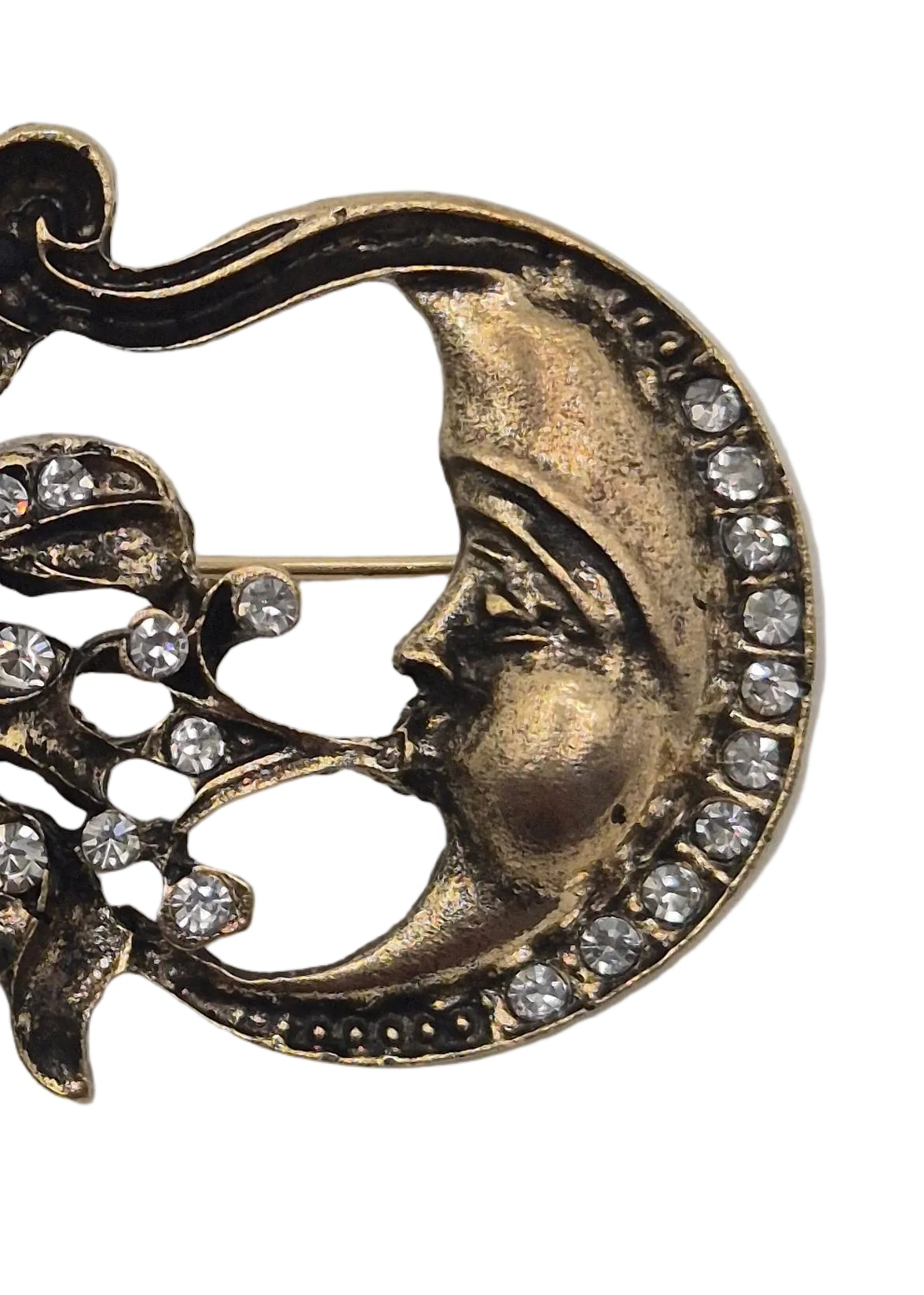 Close-up of a crescent moon brooch with a stylized face profile, accented with clear rhinestones, in an antique gold-tone metal on a white background.