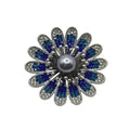 A flower-shaped brooch featuring a central gray pearl surrounded by silver-toned metal petals, with blue and clear rhinestones in each petal, set against a plain white background.