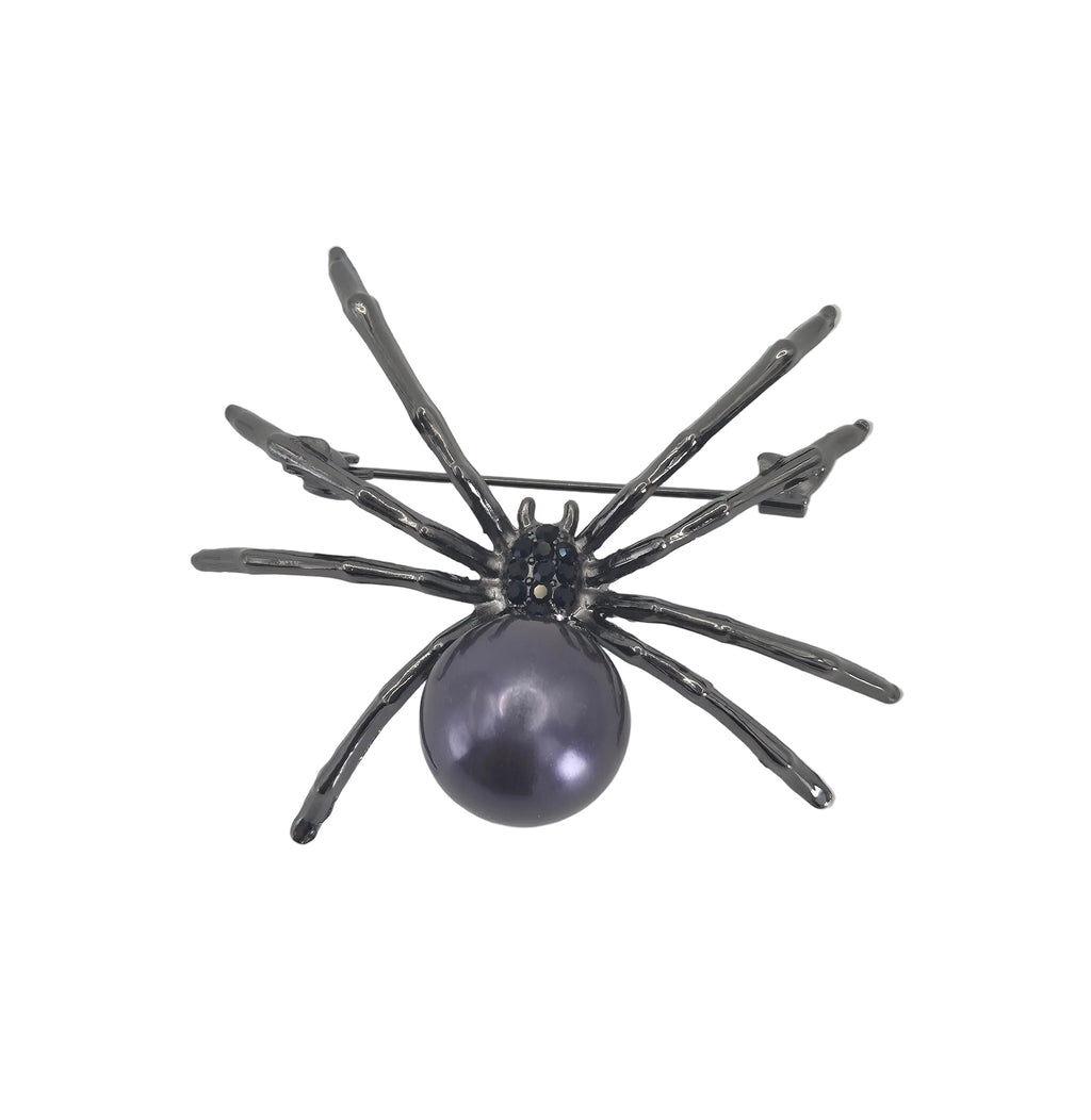 A spider-shaped brooch featuring a dark gray metallic body with a prominent oval purple pearl, photographed on a plain light gray background.