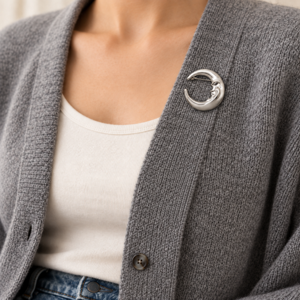 A close-up of a person wearing a gray knit cardigan over a white top, with a silver crescent moon brooch pinned on the chest.