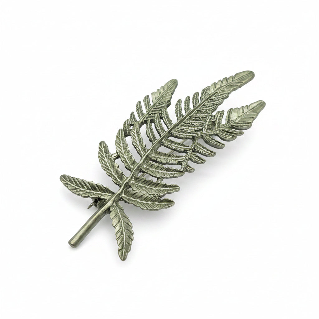 Green fern leaves brooch placed at an angle on a plain white background. 