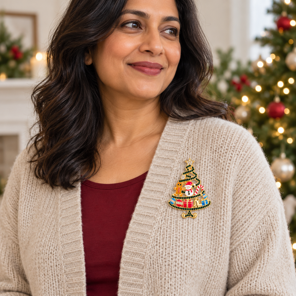 A woman wearing a beige knit cardigan over a burgundy top, featuring a colorful embroidered Christmas tree brooch on the chest, with a softly blurred holiday tree in the background.