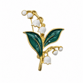 Gold lily of the valley flower brooch with green enamel leaves and white enamel bell-shaped flowers on a plain white background.