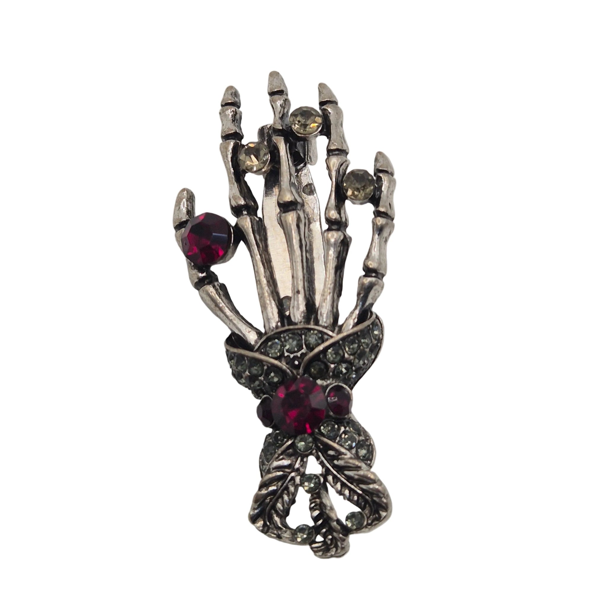 A gothic-style skeleton hand brooch featuring silver-toned metal with dark oxidized details, accented by red gemstones and small clear rhinestones, shown on a plain white background.