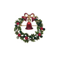 A Christmas wreath brooch with a gold-tone metal base, decorated with green holly leaves, red berries, clear rhinestones, and a central red bell with a red bow at the top.