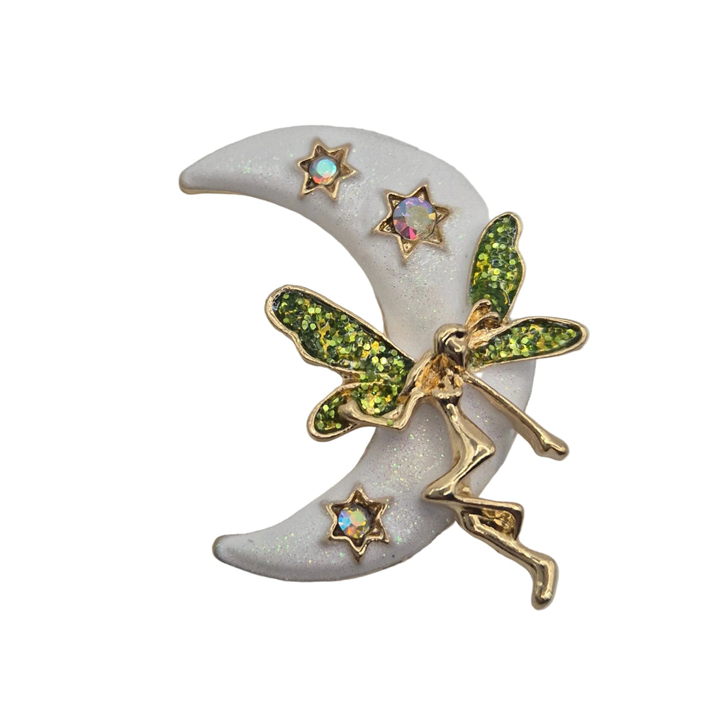 A fairy and crescent moon brooch featuring a gold-toned fairy with glittery green wings, set against a white crescent moon with small iridescent star accents, on a plain white background.