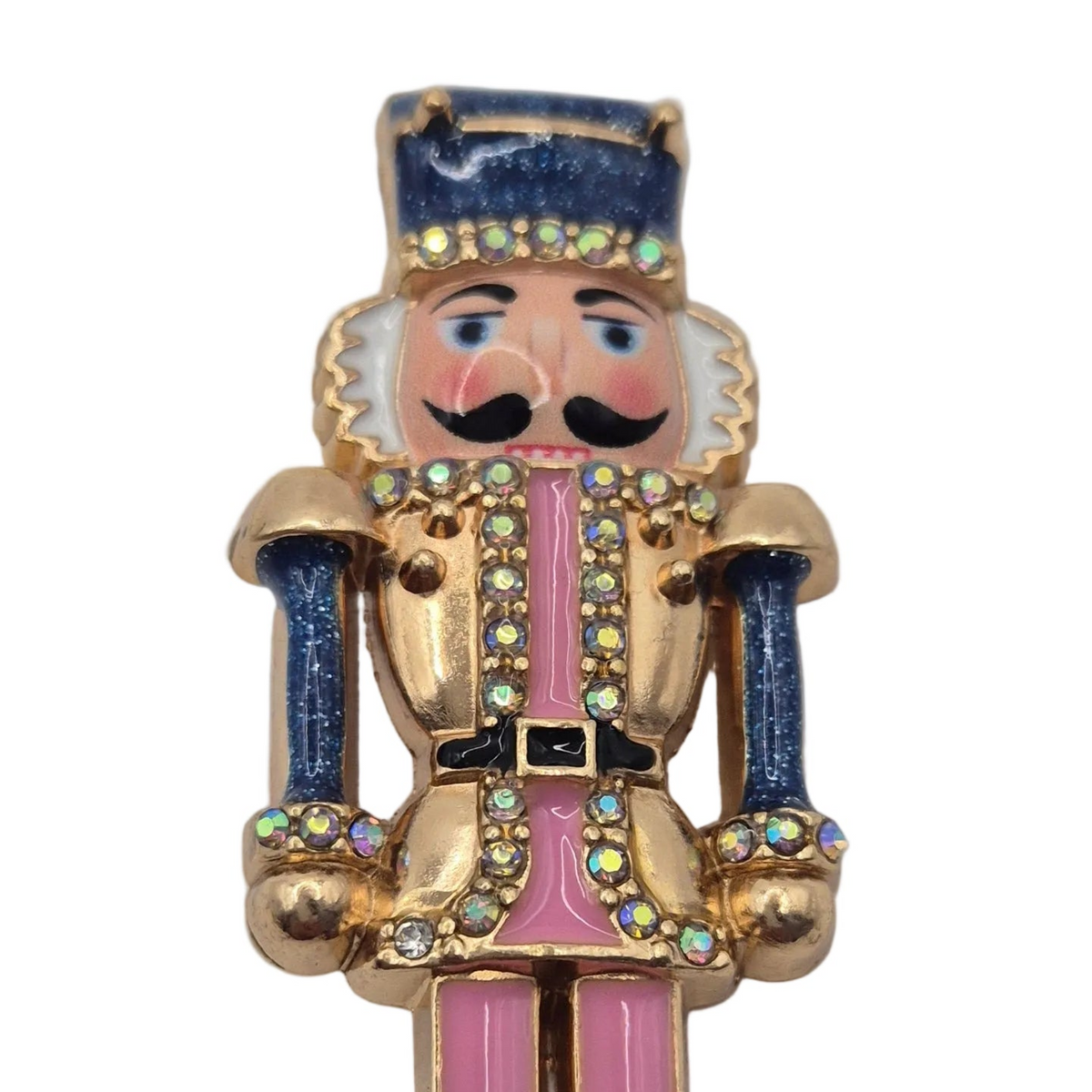 A gold-tone nutcracker figure accessory embellished with pink enamel, blue glitter accents, and iridescent rhinestones, shown against a plain white background.