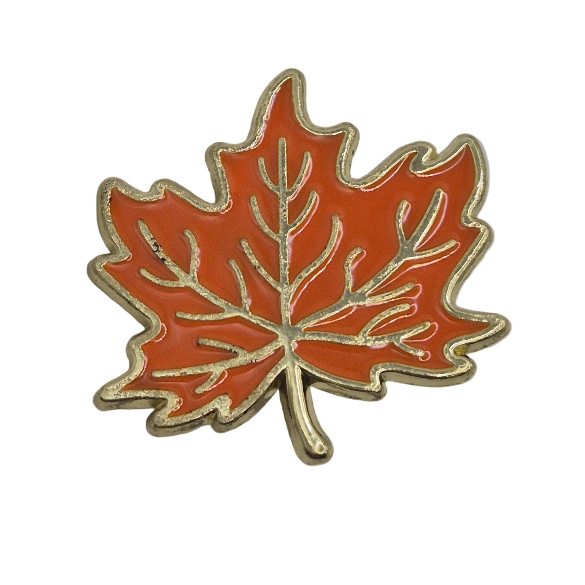 An orange maple leaf enamel pin with gold-toned metal outlines and vein details, shown on a plain white background.