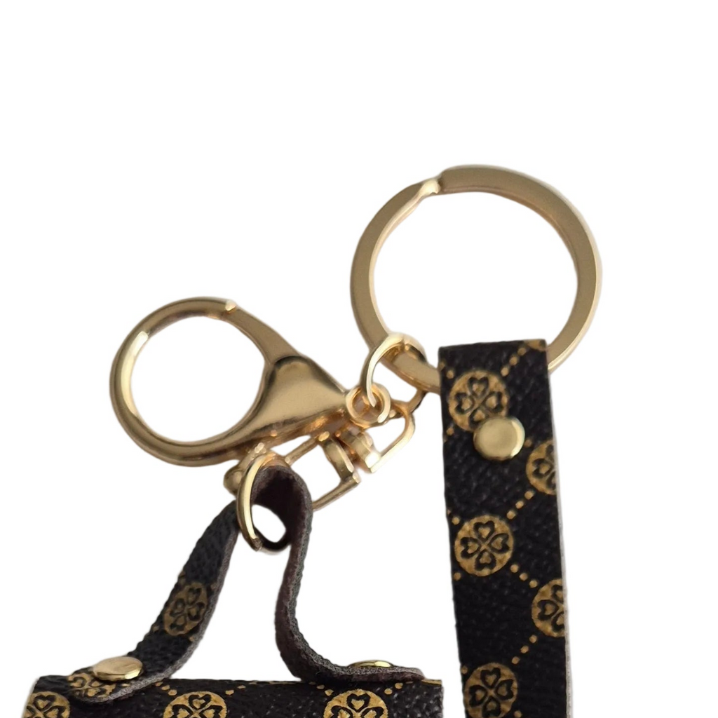 Close-up of a brown monogram keychain with gold-tone hardware, including a lobster clasp, key rings, and a matching wristlet strap on a white background.