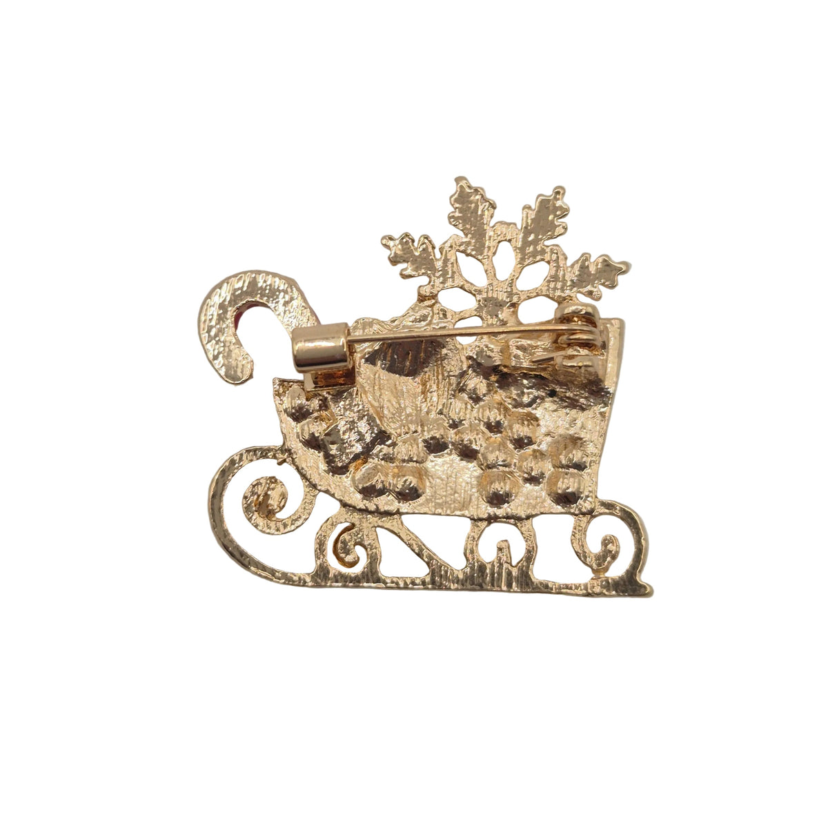 A gold-toned Christmas-themed brooch shaped like a sleigh carrying a candy cane and snowflake, photographed on a white gray background.