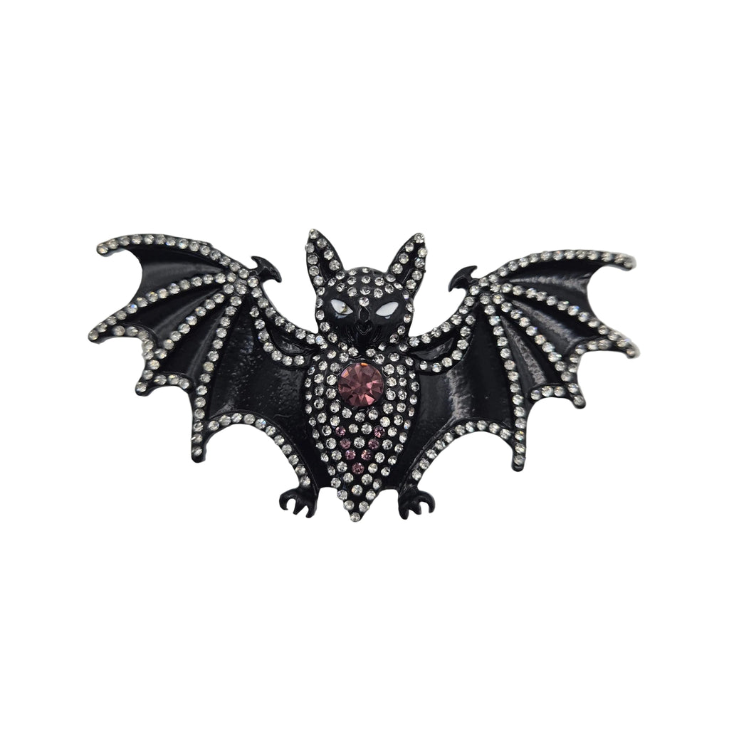 A gothic-style bat brooch or pin featuring a black enamel body, silver rhinestone-embellished wings and outline, and a small red gemstone at the centre, shown on a plain white background.