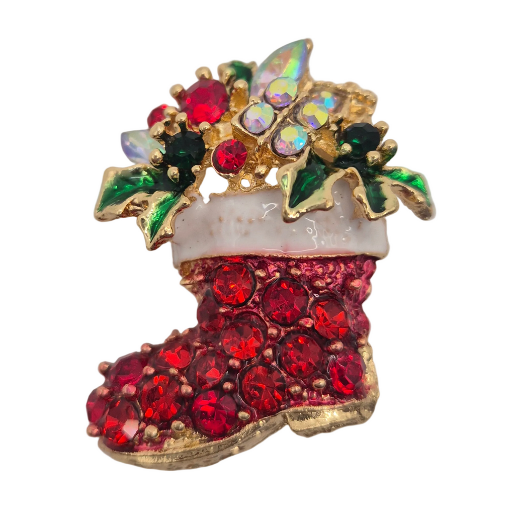 A Christmas stocking brooch featuring red rhinestones on the boot, a white faux-fur cuff, green and iridescent crystal holly leaves, and gold-tone metal outlines, shown on a plain white background.