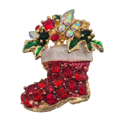 A Christmas stocking brooch featuring red rhinestones on the boot, a white faux-fur cuff, green and iridescent crystal holly leaves, and gold-tone metal outlines, shown on a plain white background.