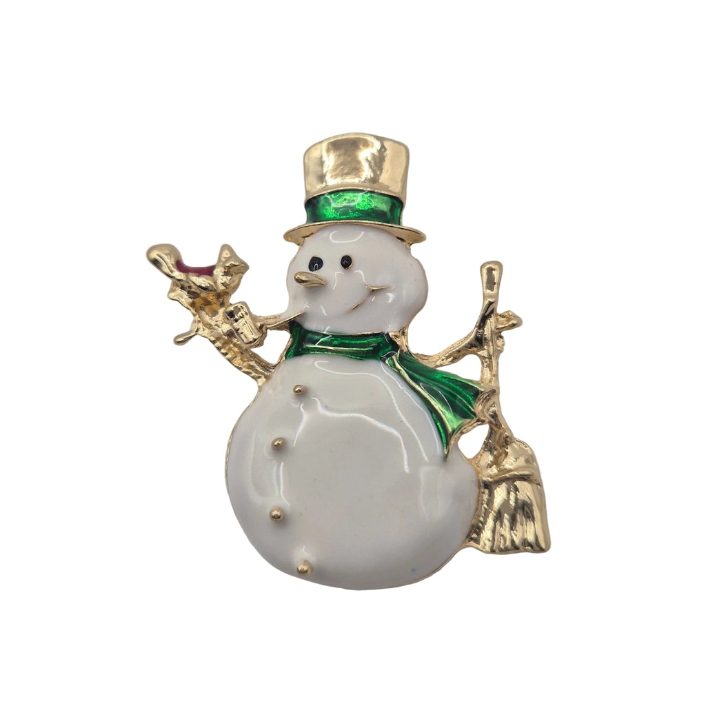 A snowman-shaped brooch with a white enamel body, gold-tone metal trim, a green scarf, and a gold top hat, holding a small gold broom.