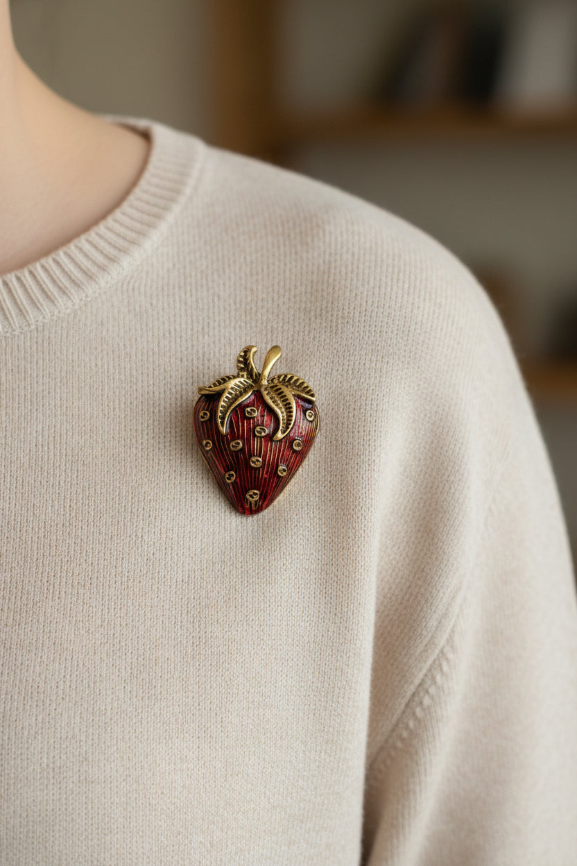 Red strawberry-shaped brooch with gold accents on a white background