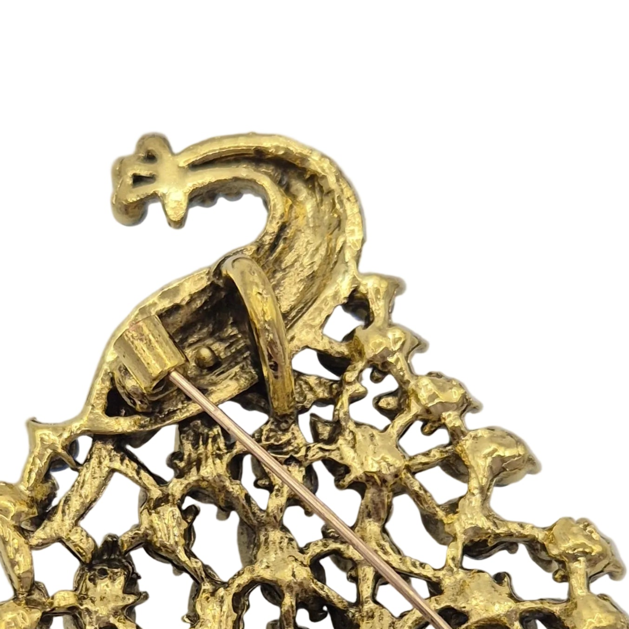 Close-up of gold reverse side of peacock brooch on a plain white background.