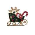 A Christmas-themed brooch featuring a gold-tone sleigh decorated with green rhinestones, red gem accents, a red-and-white striped candy cane, and a gold snowflake on a plain light background.