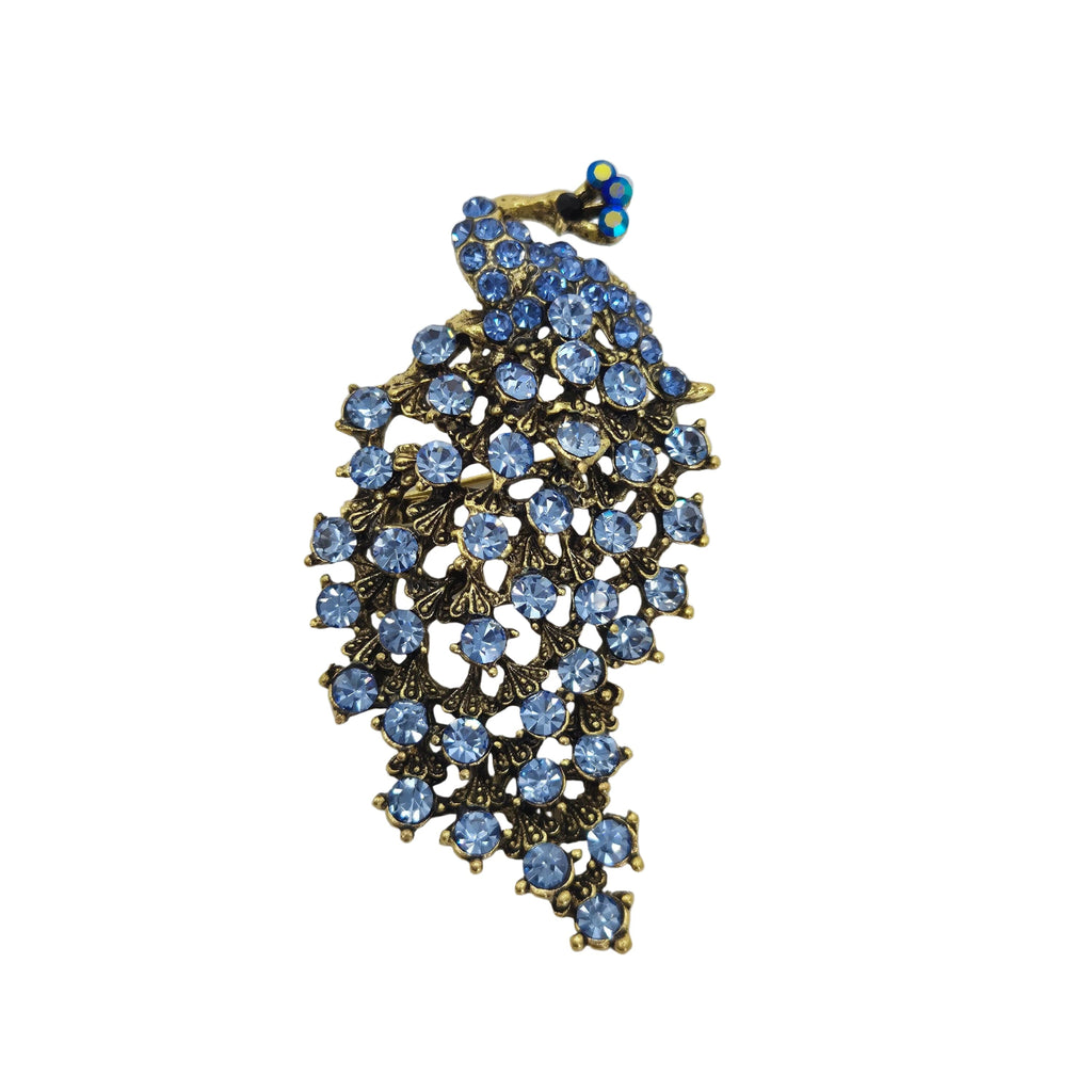 A vintage-style brooch featuring a peacock motif adorned with light blue rhinestones and gold-toned metal, set against a plain white background.