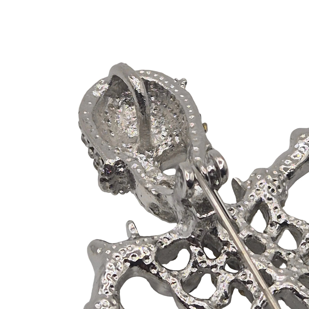 Close-up of a silver-toned skeleton brooch with a pin fastener visible, photographed on a plain white background.