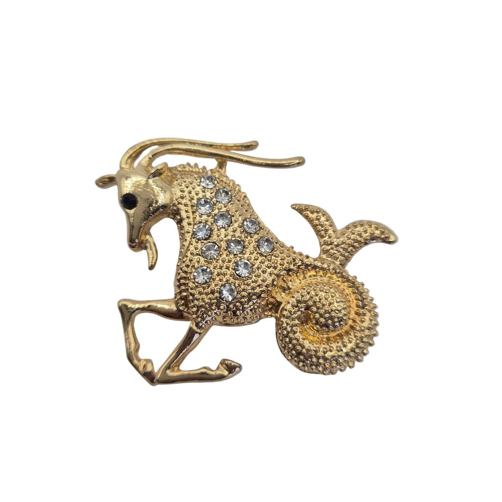 A gold-toned zodiac sign brooch shaped like a goat or ram, embellished with clear rhinestones on a plain white background.