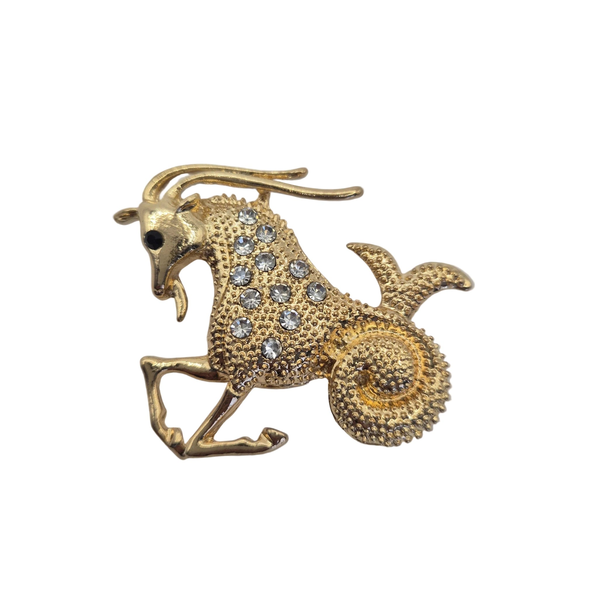 A gold-toned zodiac sign brooch shaped like a goat or ram, embellished with clear rhinestones on a plain white background.