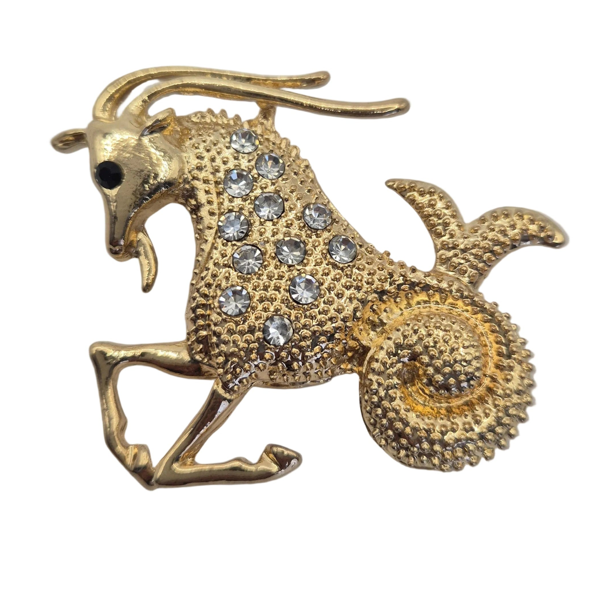 A gold-toned zodiac sign brooch shaped like a goat, embellished with clear rhinestones on its body and a small black stone for the eye, set against a plain white background.