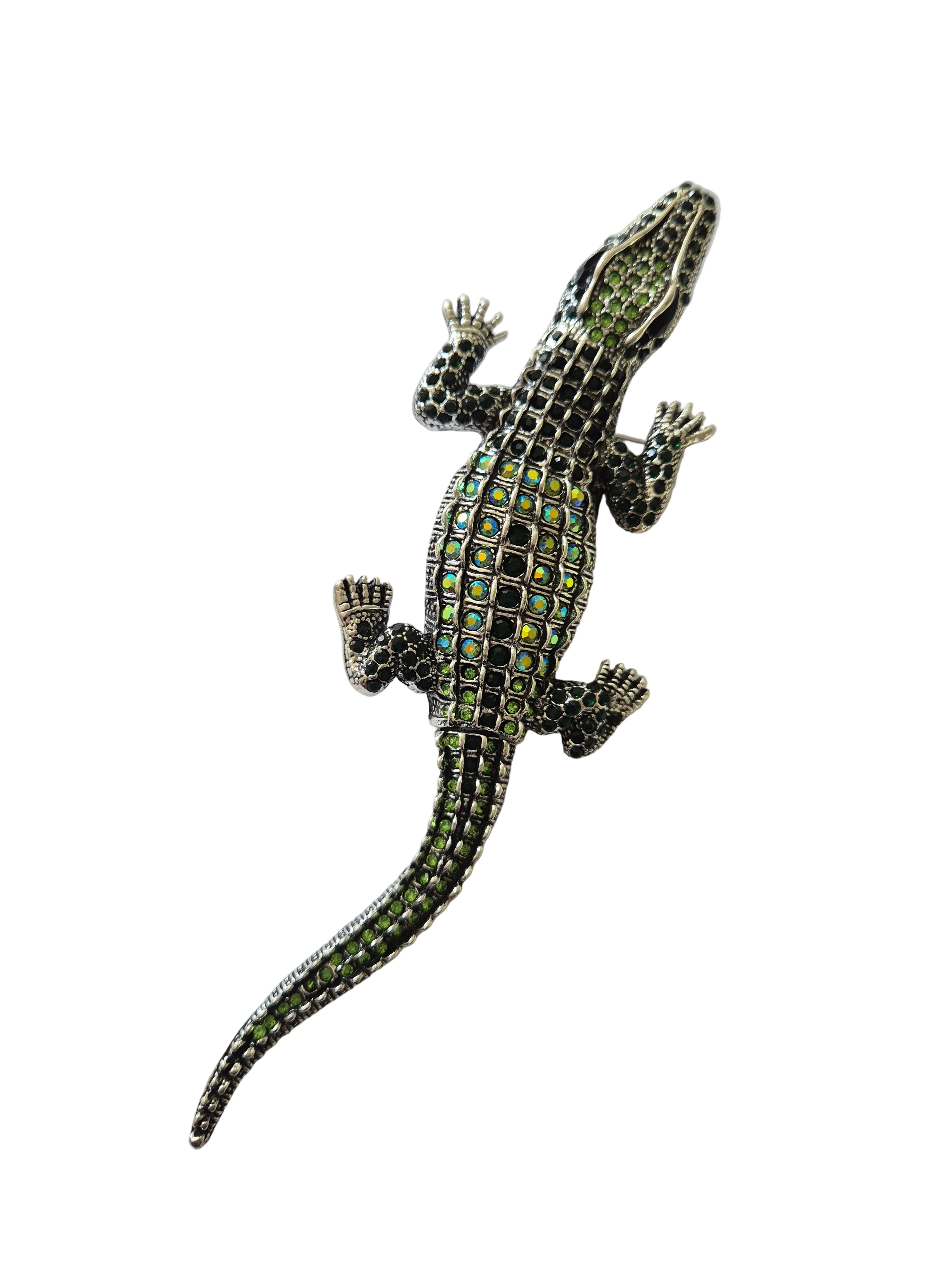 Silver crocodile brooch with green gemstones on a white background