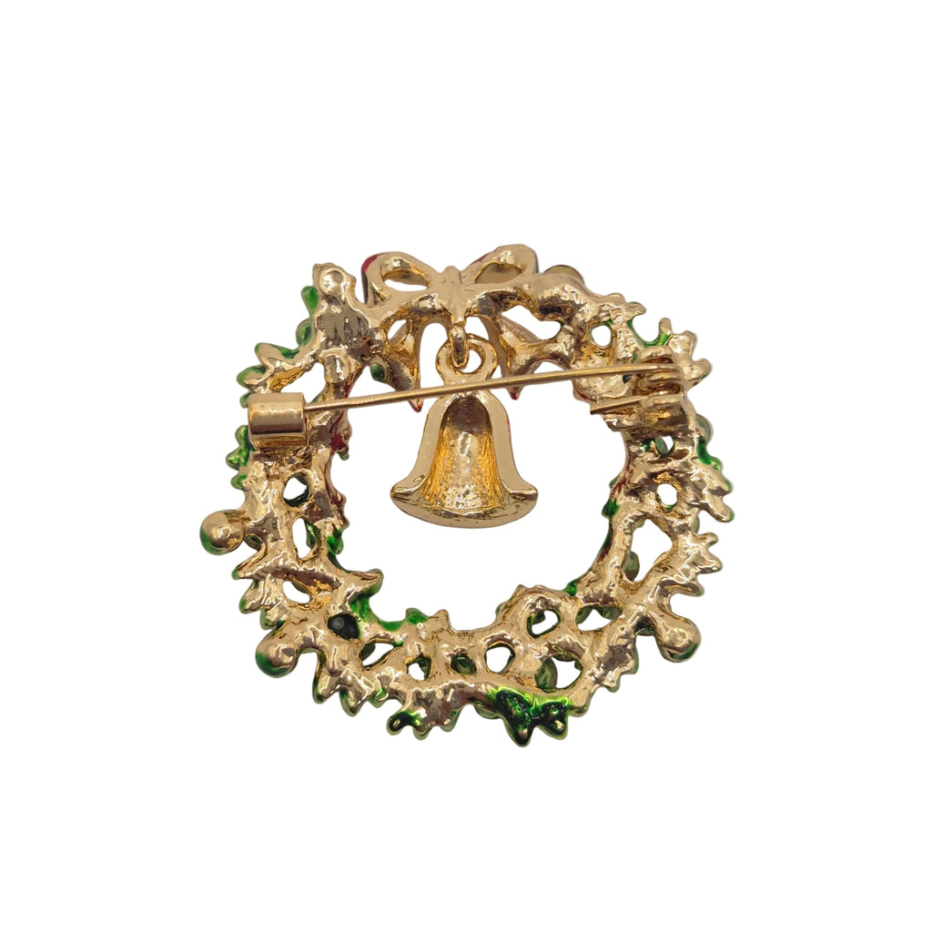 A vintage gold-tone Christmas wreath brooch with a small hanging bell and green enamel accents, shown on a plain white background.