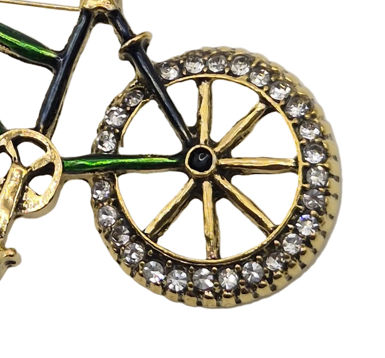 A close-up of a bicycle-themed brooch with a gold-tone metal frame, black enamel details, green accents, and clear rhinestones around the wheel, shown on a white background.