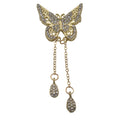 Gold butterfly brooch embellished with clear rhinestones, featuring two dangling chain drops with teardrop-shaped rhinestone charms, set against a plain light gray background.