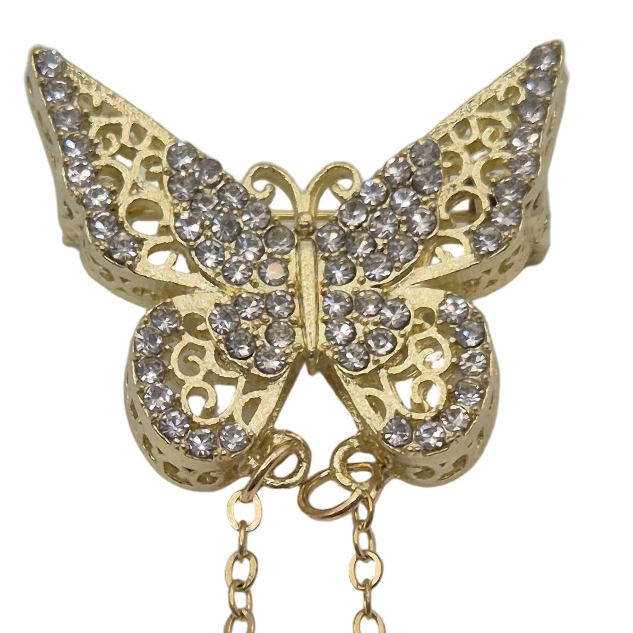 Gold butterfly-shaped brooch or pin embellished with clear rhinestones, featuring an openwork filigree design and a dangling chain, shown on a plain white background.