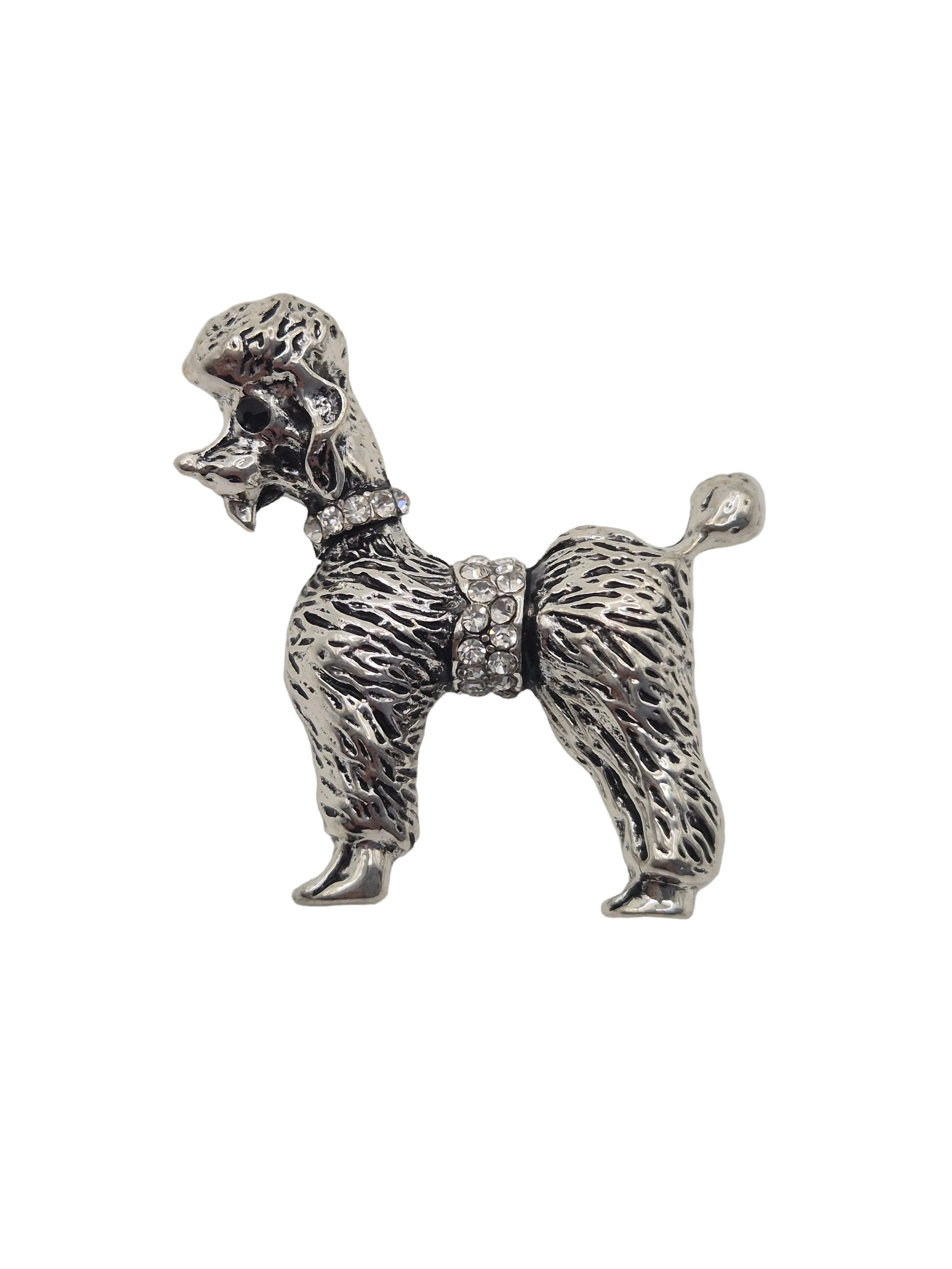 A silver-tone metal dog-shaped brooch or pin with textured fur detailing and a small rhinestone belt, shown on a plain white background.