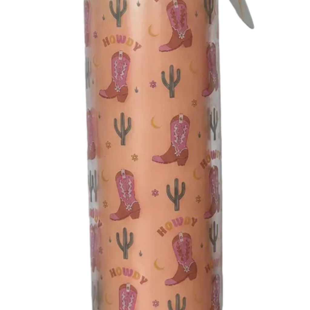 A close-up of a glass tube candle featuring a western print with pink cowboy boots, cacti, crescent moons, and the word 'HOWDY'.