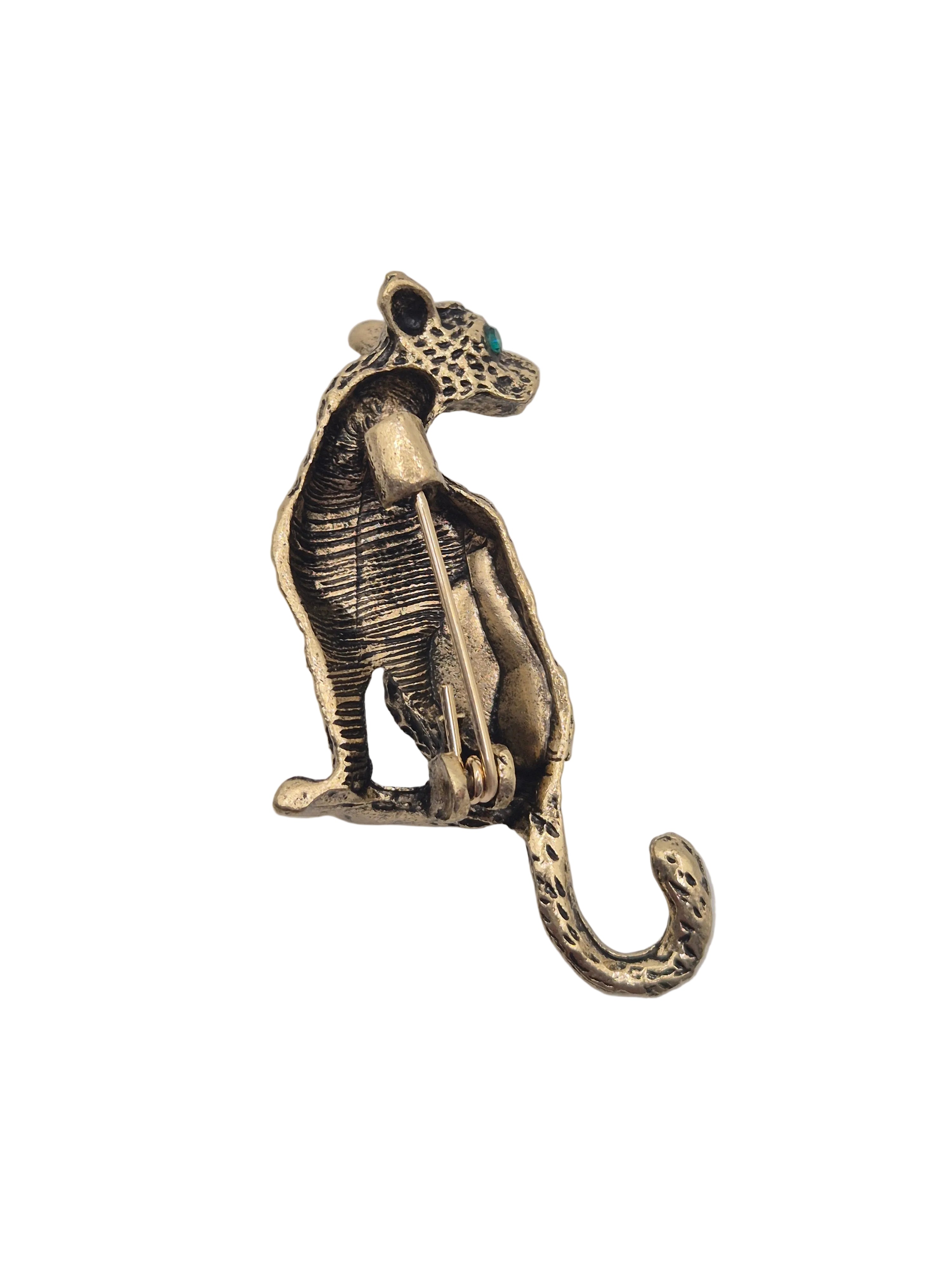 An antique bronze-colored metal leopard-shaped brooch with small green enamel eyes, shown against a plain white background.