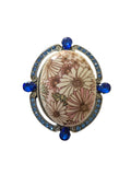 Decorative brooch with floral design and blue accents on a white background