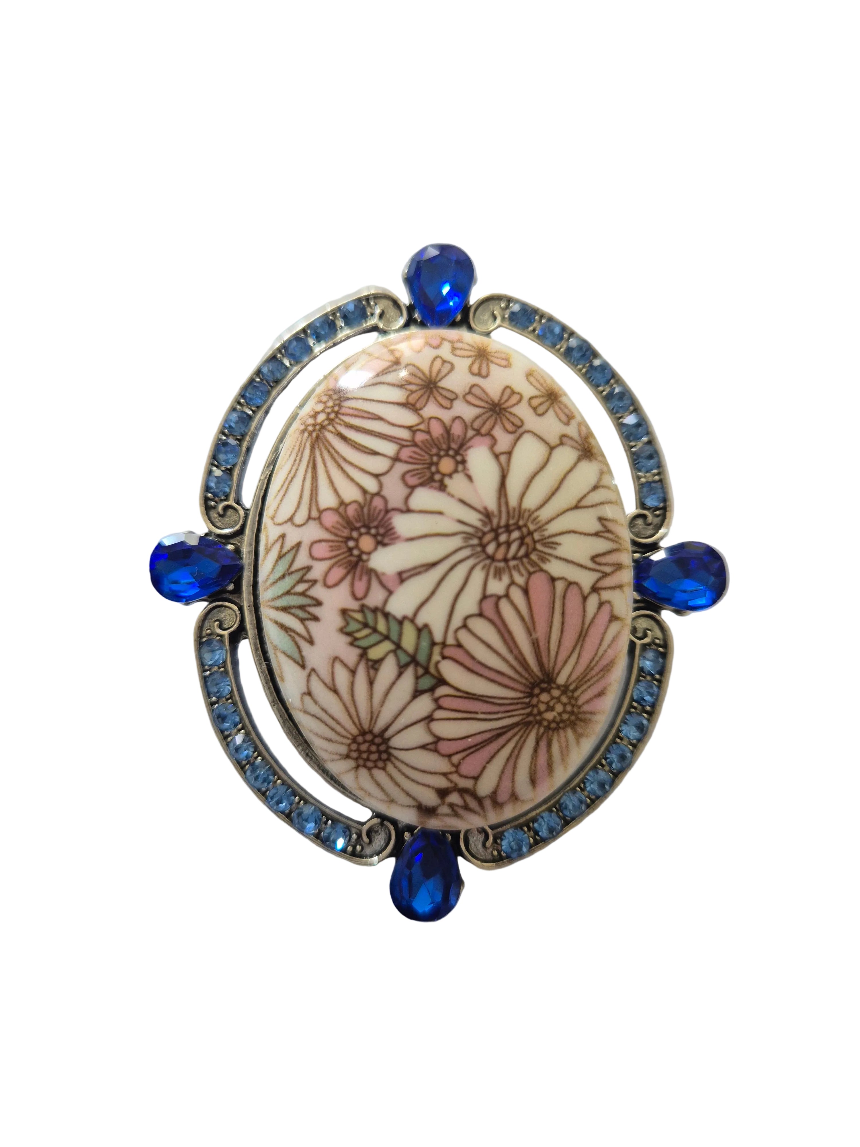 Decorative brooch with floral design and blue accents on a white background