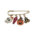 A gold-tone safety pin brooch with four Halloween-themed enamel charms: a white skull, a pink coffin, an orange jack-o'-lantern, and a black haunted house, displayed on a white background.