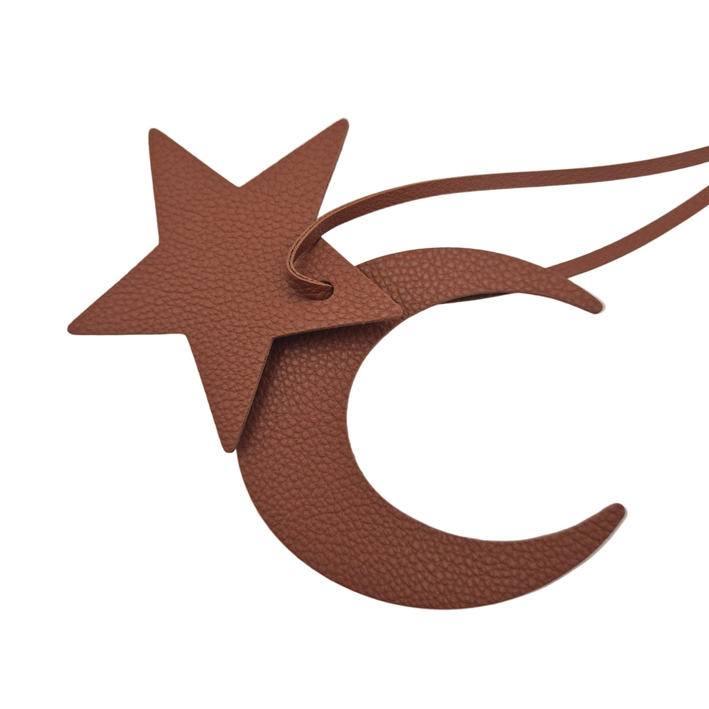 A brown textured leather star and crescent moon bag charm with a hanging loop, shown on a plain white background.