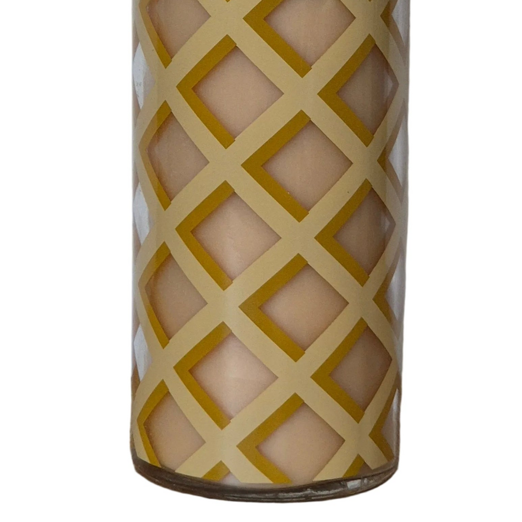 A close-up of a cylindrical glass candle holder with a geometric diamond lattice pattern, showing a beige wax candle inside against a white background.